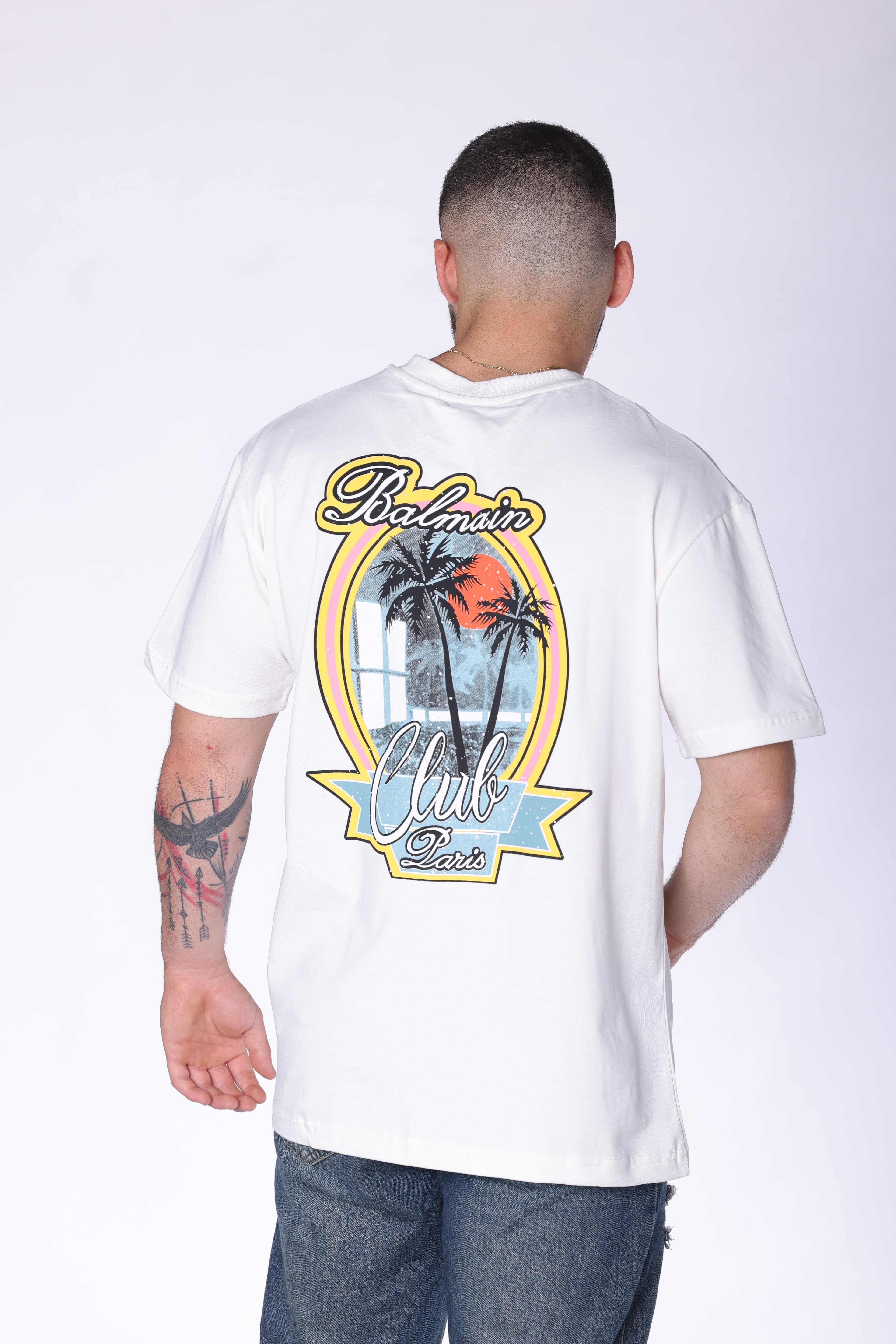 White Balmain Club Oversized T-Shirt - Premium white oversized t-shirt featuring a minimal front chest logo and bold Balmain Club Paris-inspired artwork on the back with tropical sunset design details. Made from soft breathable fabric with a relaxed fit for everyday comfort. A standout luxury streetwear piece perfect for summer outfits, casual styling, and elevated everyday wear.