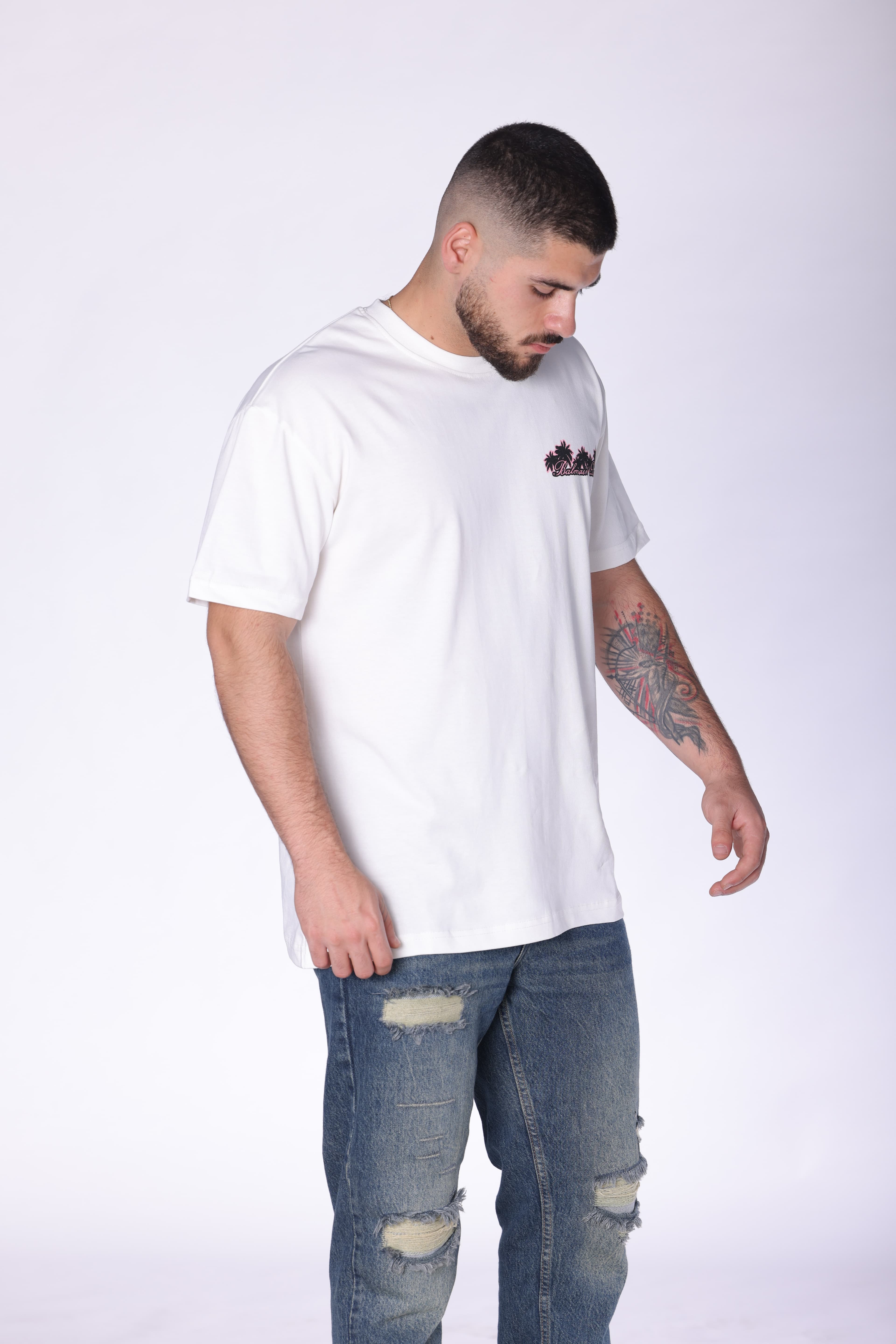 White Balmain Club Oversized T-Shirt - Premium white oversized t-shirt featuring a minimal front chest logo and bold Balmain Club Paris-inspired artwork on the back with tropical sunset design details. Made from soft breathable fabric with a relaxed fit for everyday comfort. A standout luxury streetwear piece perfect for summer outfits, casual styling, and elevated everyday wear.