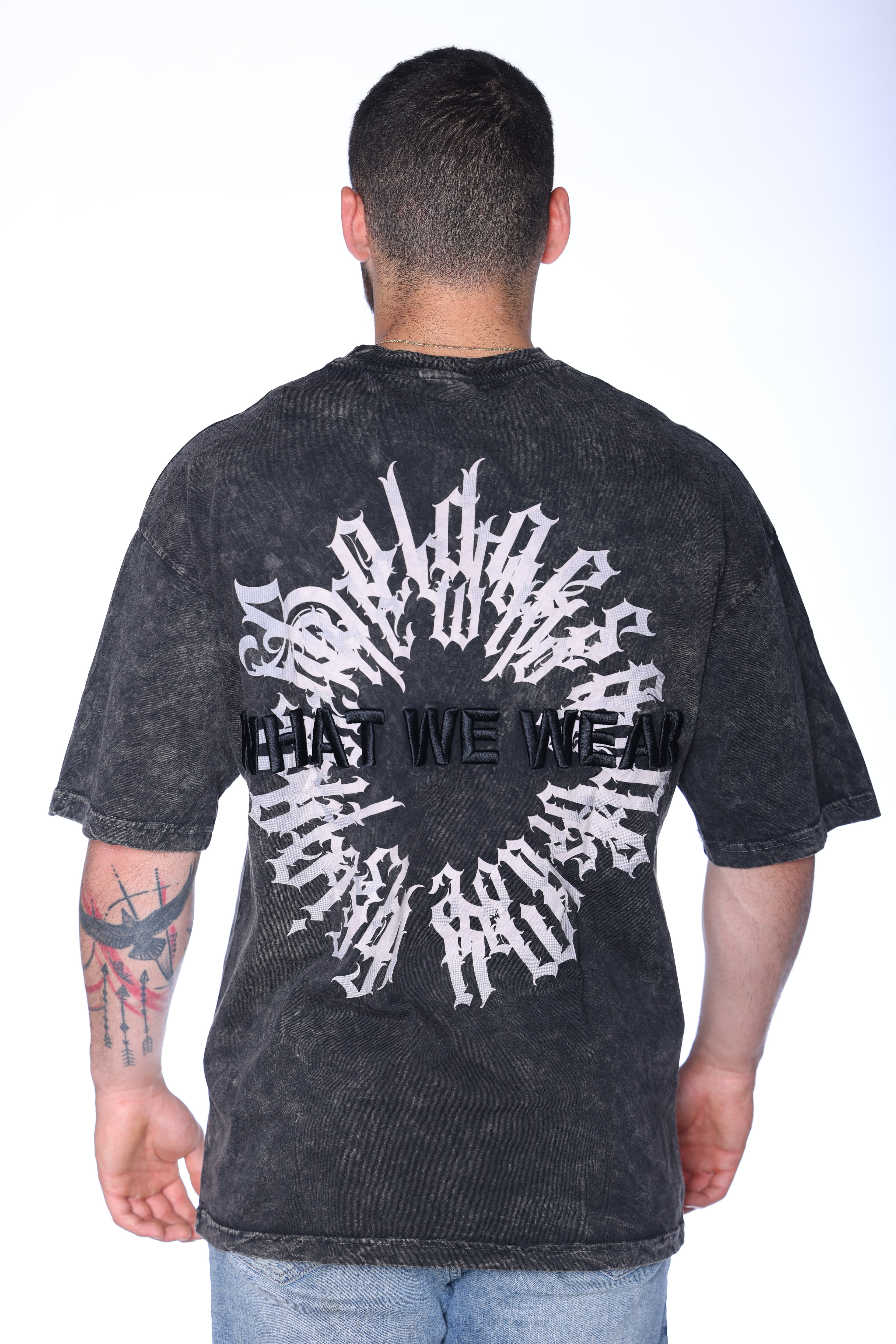 Vintage Charcoal Washed T-Shirt Oversized - Oversized washed black t-shirt featuring a subtle front chest graphic and bold gothic statement artwork on the back with raised What We Wear text detail. Crafted from soft premium fabric with a vintage faded finish and relaxed fit for all-day comfort. A standout streetwear essential perfect for edgy casual looks, layered outfits, and everyday wear.