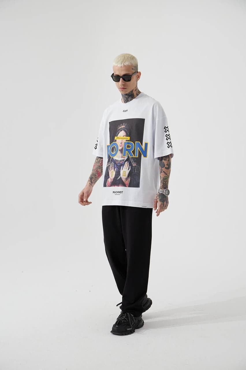 Oversized White Graphic T-Shirt "born" - Oversized white graphic t-shirt featuring a bold vintage-inspired front print with artistic portrait artwork and standout “BORN” lettering in blue with yellow outline. Designed with sleeve cross symbols on both sides and subtle chest detailing for a streetwear edge. Made with a relaxed drop-shoulder fit and soft cotton fabric, perfect for everyday casual looks.
