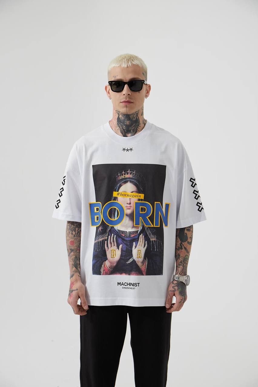 Oversized White Graphic T-Shirt "born" - Oversized white graphic t-shirt featuring a bold vintage-inspired front print with artistic portrait artwork and standout “BORN” lettering in blue with yellow outline. Designed with sleeve cross symbols on both sides and subtle chest detailing for a streetwear edge. Made with a relaxed drop-shoulder fit and soft cotton fabric, perfect for everyday casual looks.