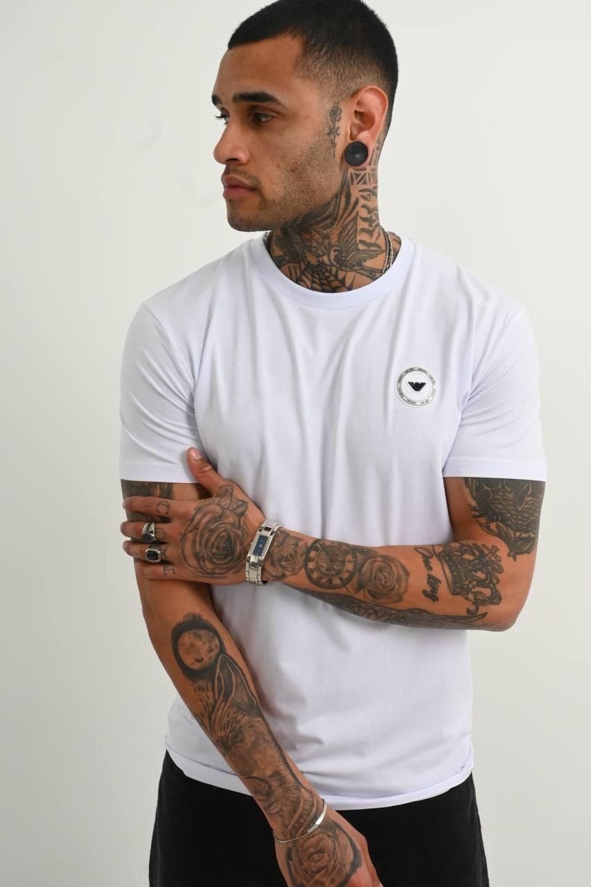 Classic White Premium Tee - Classic white premium tee with a clean minimal design and sleek chest emblem detail. Crafted with a smooth soft-touch fabric and a fitted cut that gives a sharp modern look. Easy to style for both streetwear and casual outfits, whether layered or worn on its own. Timeless, versatile, and made for an everyday luxury vibe.